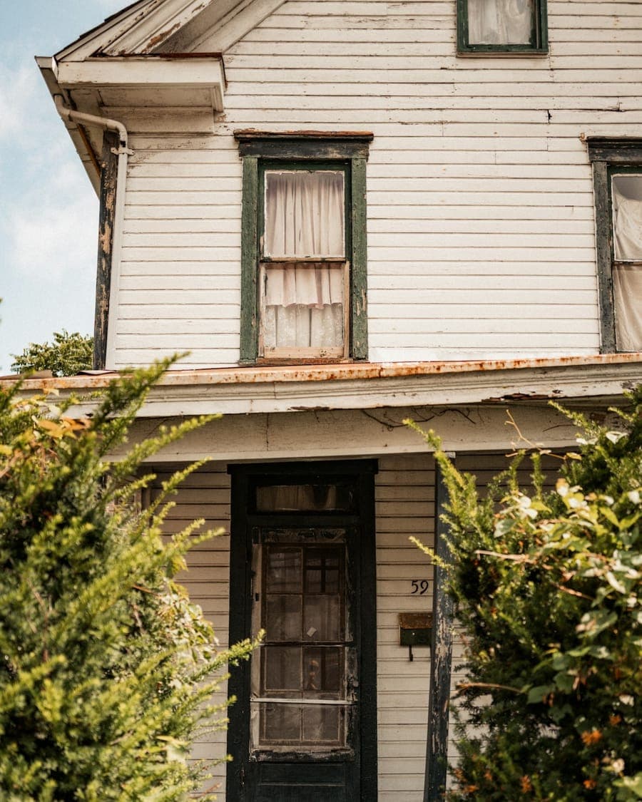 Photo of an old house with peeling window trim and a worn front door